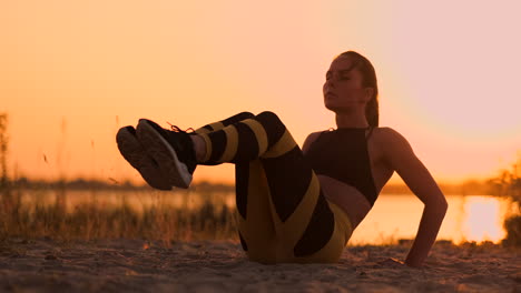 Junge-Schöne-Sportlerin,-Die-Am-Strand-Bei-Sonnenuntergang-Übungen-Für-Die-Bauchmuskulatur-Macht-Und-Sich-In-Zeitlupe-Dreht